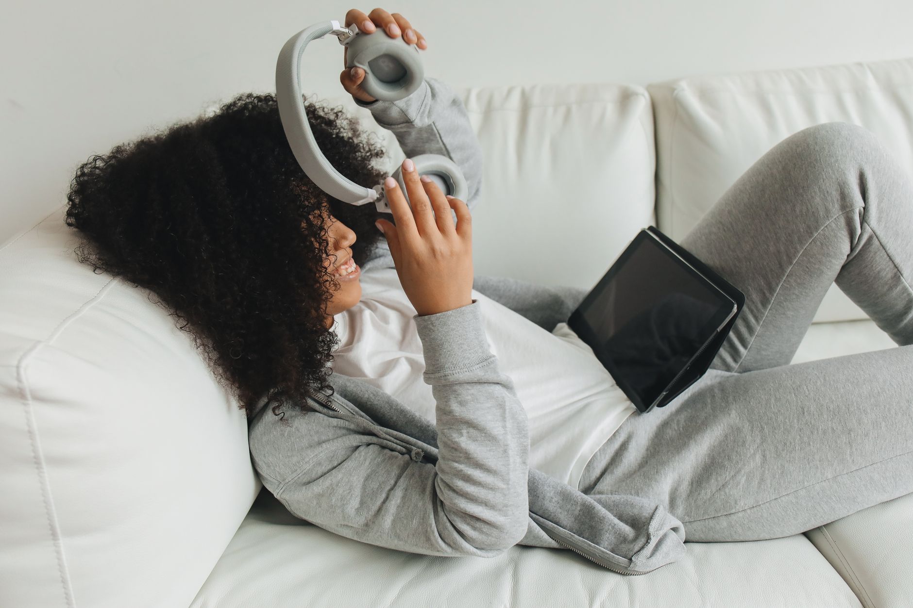 Woman relaxing at home with headphones and a tablet, reviewing work from her couch.