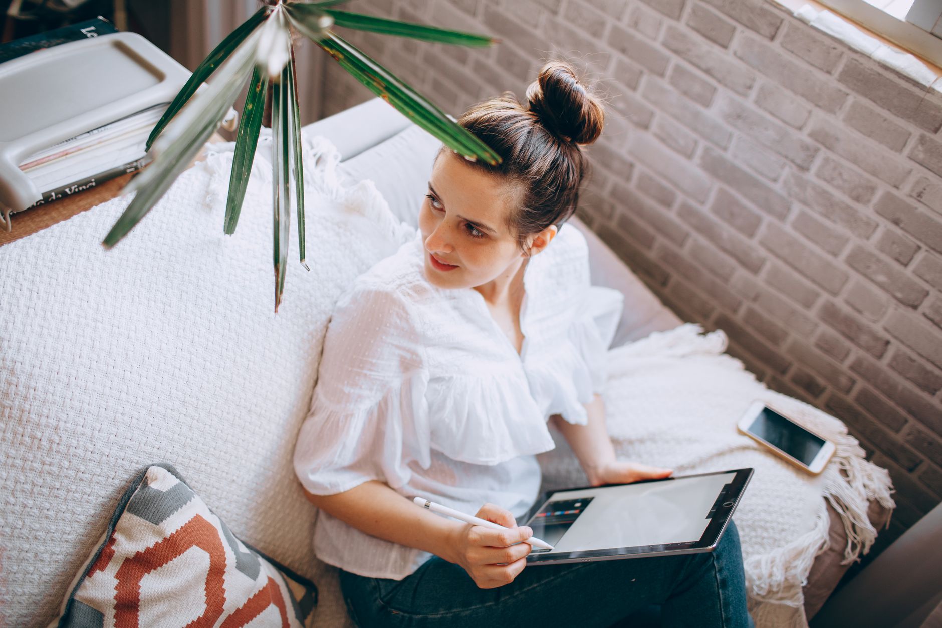 Overhead view of a woman using a tablet and stylus on the sofa while planning her work.